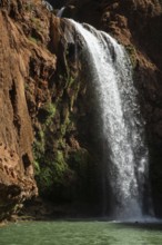 Moroccan young man jumps from the high rock into the water under a waterfall Ouzoud