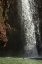 Moroccan young man jumps from the high rock into the water under a waterfall Ouzoud