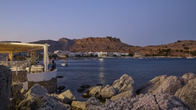 Feraklos fortress, view of an illuminated coastal town at night with rocks in the foreground, bay,