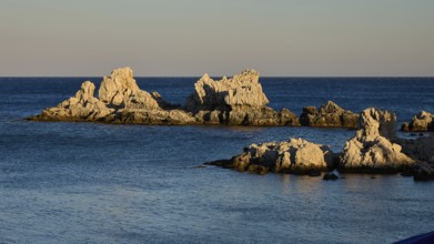 Large rock formations rise out of the calm blue sea under the soft evening light, Charaki Bay,