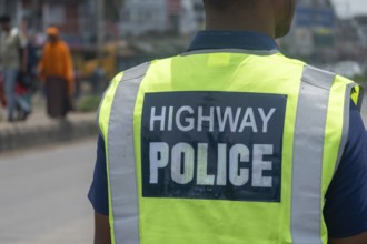Officer in a reflective vest standing roadside, ensuring safety in urban area, Dhaka, Bangladesh