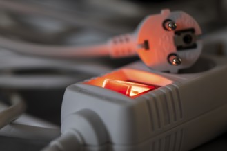 Close-up of a white power plug, Schuko plug, on a multiple socket with red indicator light,