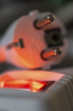 Close-up of a white power plug, Schuko plug, on a multiple socket with red indicator light,