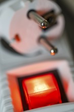 Close-up of a white power plug, Schuko plug, on a multiple socket with red indicator light,