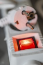 Close-up of a white power plug, Schuko plug, on a multiple socket with red indicator light,