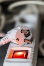 Close-up of a white power plug, Schuko plug, on a multiple socket with red indicator light,