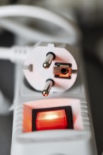Close-up of a white power plug, Schuko plug, on a multiple socket with red indicator light,