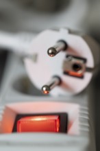 Close-up of a white power plug, Schuko plug, on a multiple socket with red indicator light,