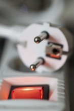 Close-up of a white power plug, Schuko plug, on a multiple socket with red indicator light,