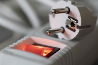 Close-up of a white power plug, Schuko plug, on a multiple socket with red indicator light,