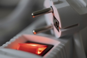 Close-up of a white power plug, Schuko plug, on a multiple socket with red indicator light,
