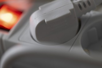 Close-up of a white power plug, Schuko plug, plugged into a multiple socket with red indicator
