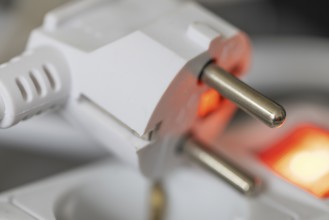 Close-up of a white power plug, Schuko plug, on a multiple socket with red indicator light,