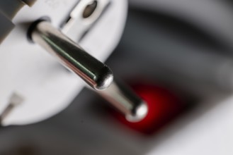 Close-up of a white power plug, Schuko plug, on a multiple socket with red indicator light,