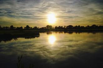 The setting sun paints the sky in warm colours that are reflected in the lake, natural landscape in