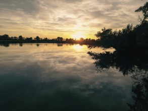 The sun sets over a calm lake and casts gentle reflections on the water, natural landscape in