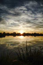 Sunset with clouds and grasses on the lakeshore reflected in the still water, natural landscape in