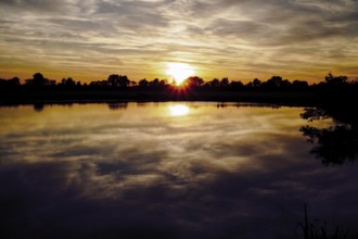 The sunset lights up the sky while the lake reflects the colours, natural landscape in Wüsting,