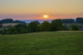 Sun rises over green meadow and wooded valley, colourful sky, Laudenau, Reichelsheim, Odenwald,