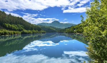 Tranquil ibiur reservoir mirrors the picturesque landscape of lush green hills and vibrant blue sky