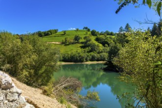 Ibiur reservoir reflects the surrounding green hills and lush vegetation under a clear blue sky,