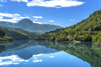 The serene ibiur reservoir in tolosa, gipuzkoa, reflects the surrounding mountains and blue sky