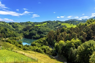 Ibiur reservoir reflects the vibrant blue sky amidst the rolling green hills and lush forests of