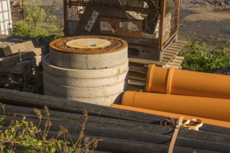 Borken, NRW, Germany, Orange and black pipes, concrete rings, and a rusty manhole cover sit at a