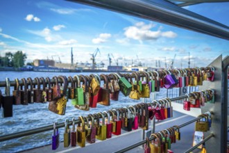 Many colourful love locks on a railing with a view of the harbour and cranes. View from the jetties