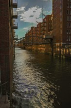 Sunlight is reflected in the water of the canal between tall brick buildings. View from the
