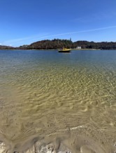 Clear water on a beach with a view of a yellow boat and wooded island in the background, Silver