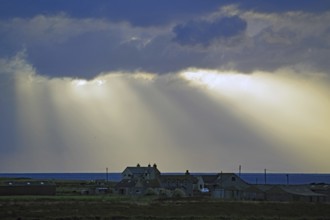 Sunbeams break through dramatic clouds over houses by the sea, John O Groats, Scotland, Great