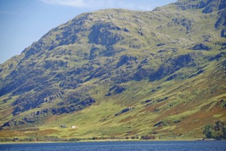 Green slopes of a large mountain with scattered farm buildings under a clear sky, Knoydart,