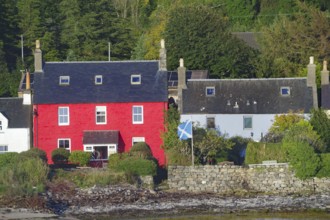 Red house with Scottish flag surrounded by trees and a stone wall in a seaside village, Dornie,