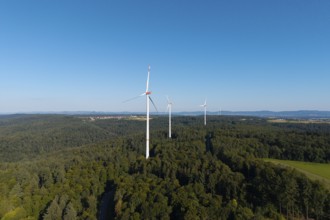 Wind turbines above green forests under a blue sky, symbolising clean energy, near Schorndorf in