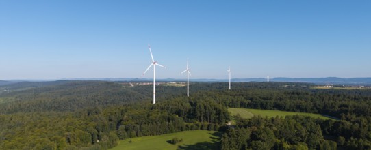Wind turbines stand above a wooded hill under a clear blue sky, near Schorndorf, Rems Valley,