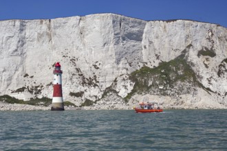 Red lighthouse and boat near white cliffs by the sea, Beachy Head Lighthouse, Bournemouth, Dorset,