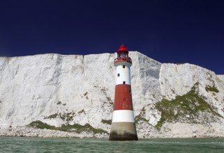 Red lighthouse in front of imposing white cliffs on the green sea, Beachy Head Lighthouse,
