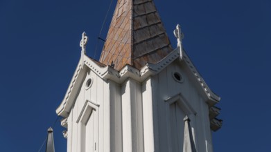 Pointed church tower with wooden elements and clear blue sky in the background, Tangen kirke or