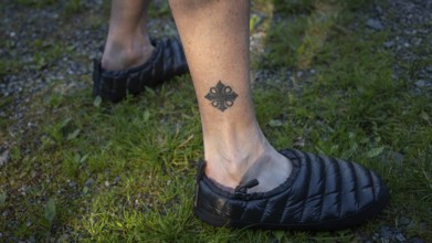 Leg tattooed with Olav's cross, pilgrim in tap shoes on grassy ground, Olavsweg or Olavsleden,
