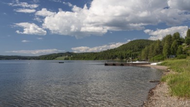 View of bathing area at Lake Mjøsa or Lake Mjosa with wooded shore under blue sky, Olavsweg or