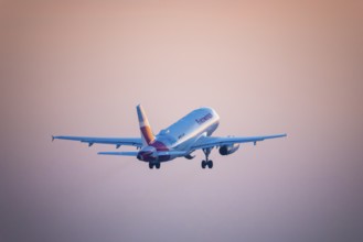 A Eurowings aeroplane takes off and disappears into an orange evening sky, Stuttgart,