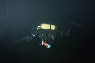 A diver in a diving suit explores a dark underwater environment. Dive site wreck of the Jura, Lake
