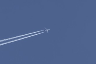 Jet passenger aircraft flying with vapour trails or contrails behind in a blue sky, England, United