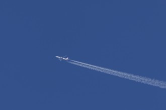 Jet passenger aircraft of American Airlines flying with vapour trails or contrails behind in a blue