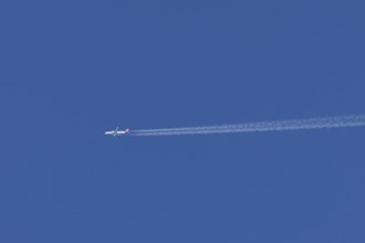 Jet passenger aircraft of Austrian Airways flying with vapour trails or contrails behind in a blue