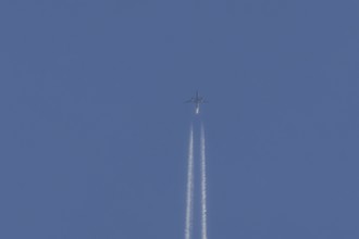 Jet passenger aircraft flying with vapour trails or contrails behind in a blue sky, England, United