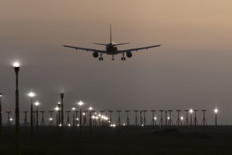 Airbus jet passenger aircraft in flight landing at sunset over runway lights at London Stansted
