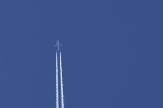 Airbus passenger jet aircraft flying with a vapour trial or contrail behind in a blue sky, England,