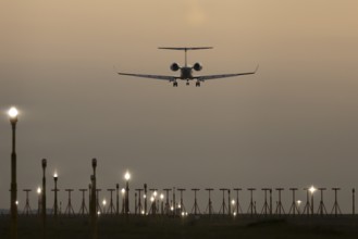 Executive business jet passenger aircraft landing over runway lights at sunset, London Stansted